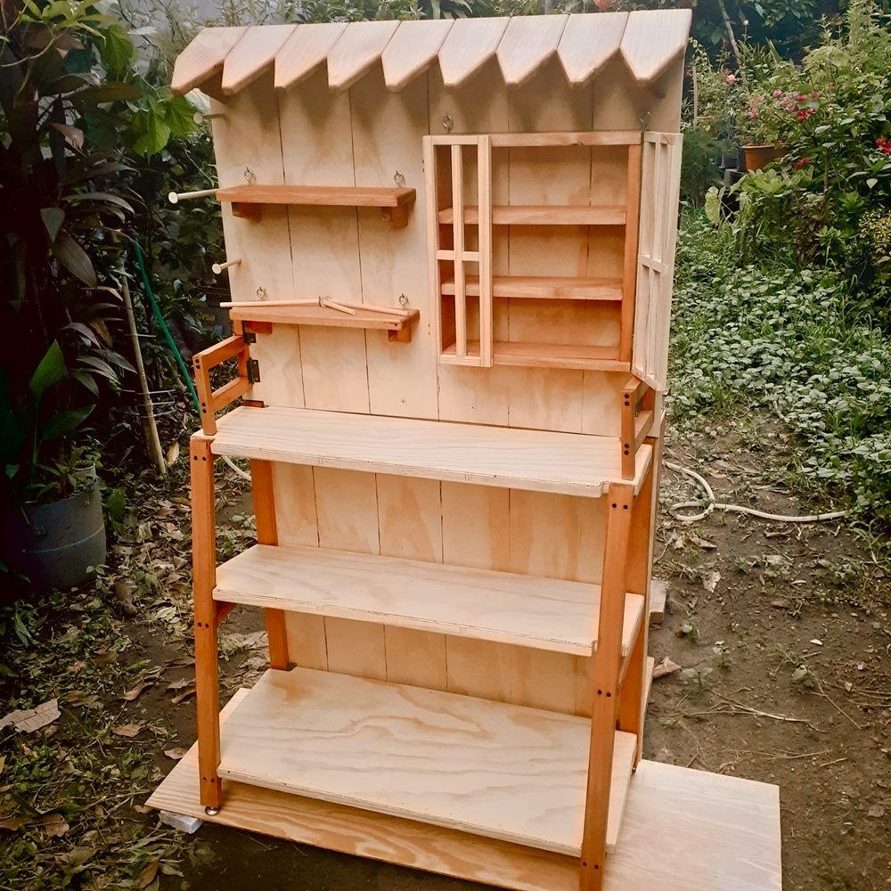 Panel Multiusos de madera armado en un jardín, con techo de tejas, repisas, vitrina y tres estantes