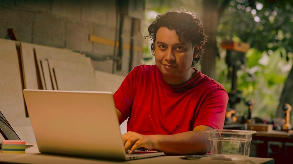 Integrante de IDEOMOV sonriendo frente a su computadora en el taller