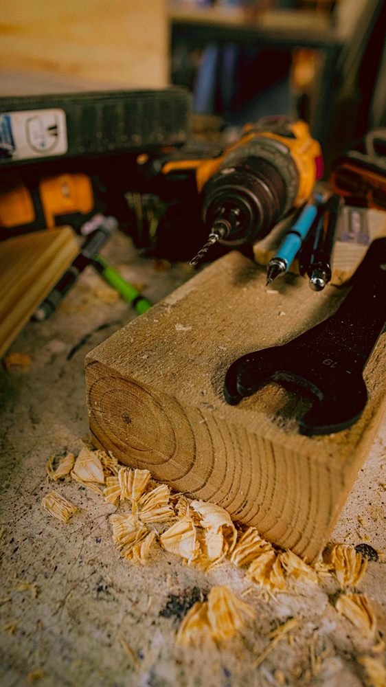 Taladro, lápices y llave sobre un bloque de madera rodeado de viruta